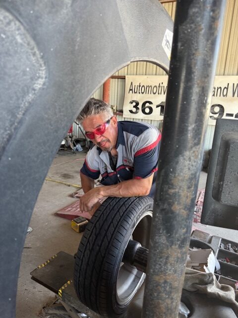 Auto technician inspecting a tire in a workshop, wearing safety glasses and working on vehicle maintenance. Relevant for automotive service content.