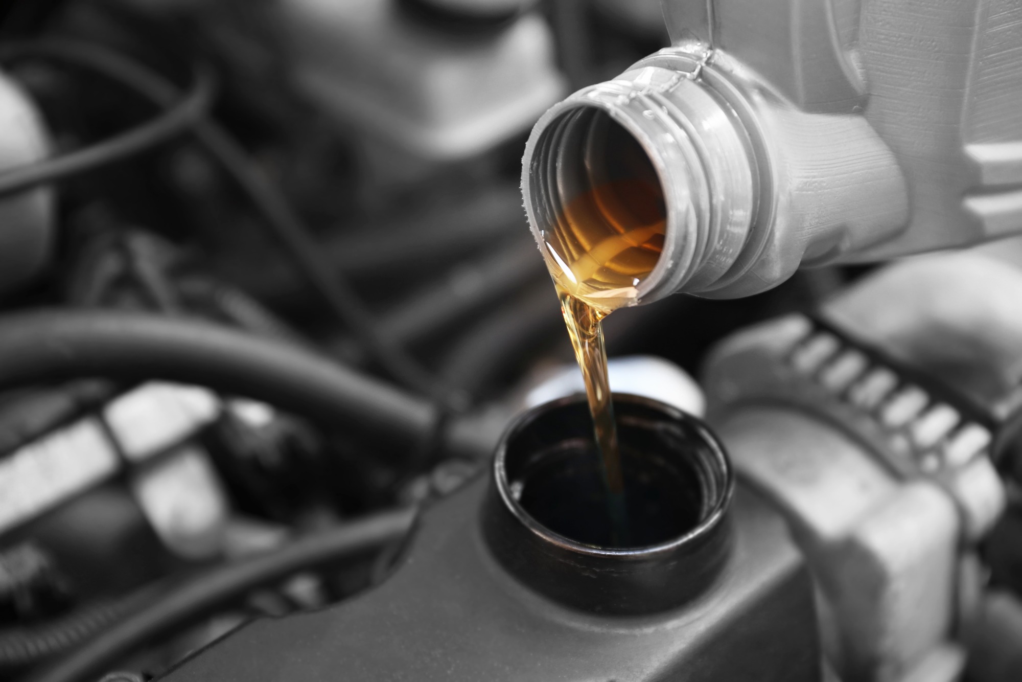 Oil is being poured from a bottle into a car's engine oil reservoir, illustrating routine vehicle maintenance.