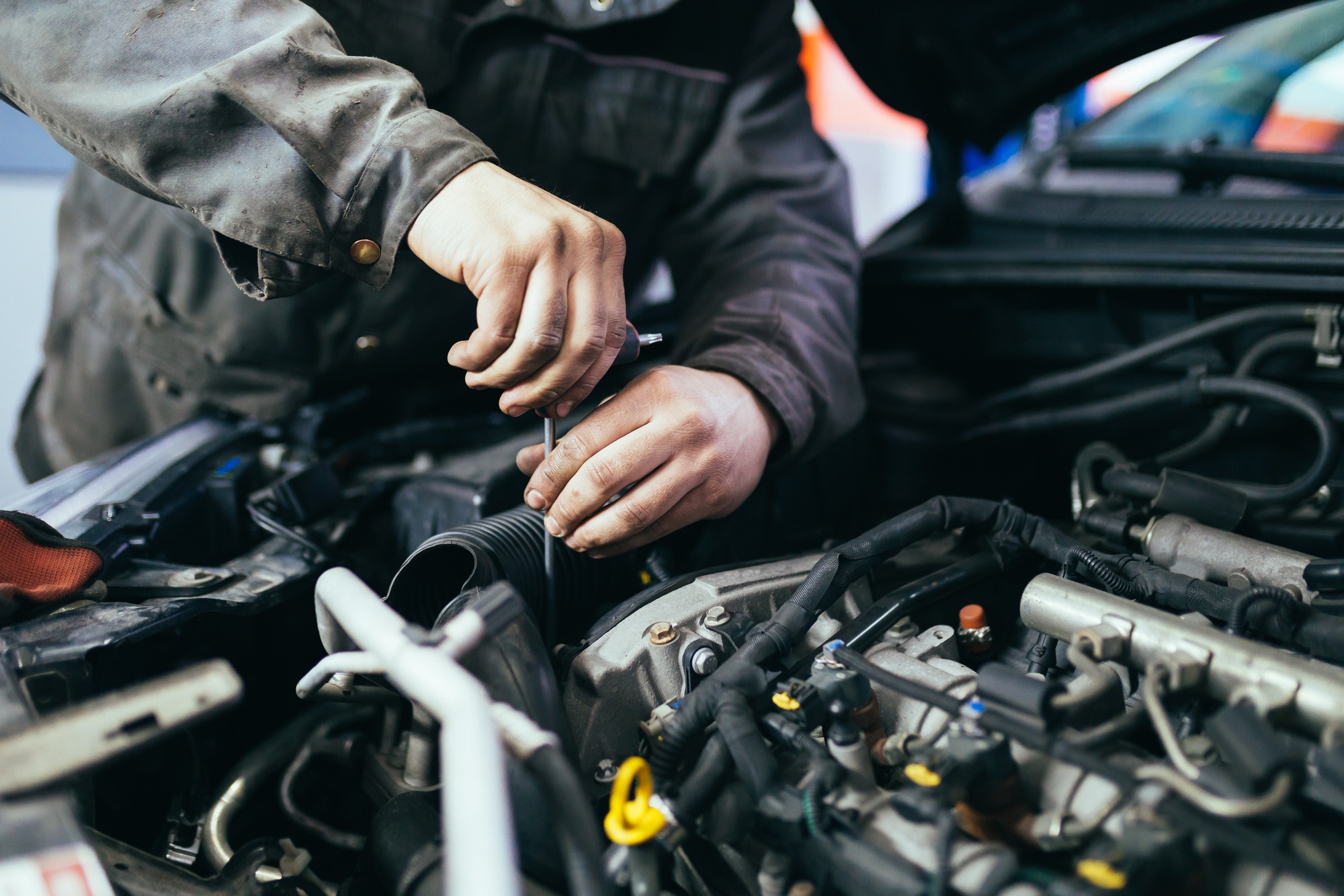 A mechanic works under the hood of a car, using a wrench to adjust an air intake component, emphasizing vehicle maintenance and repair.