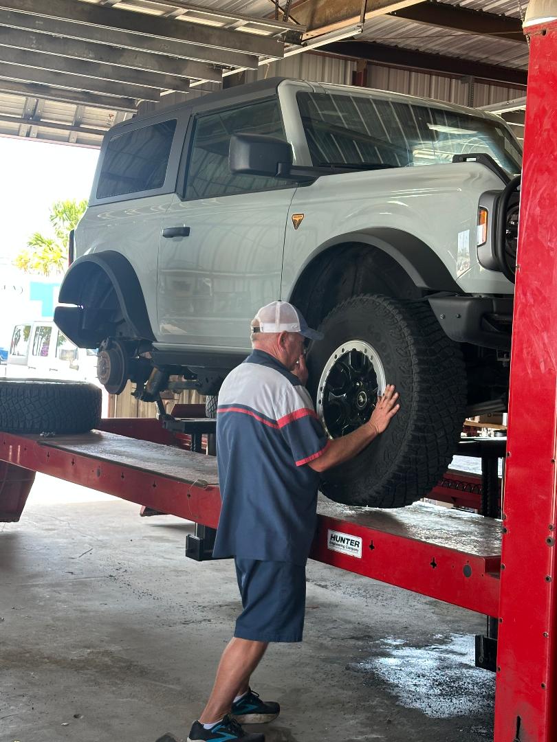 Mechanic working on a lifted gray SUV in a garage, focusing on installing a tire. The scene highlights auto maintenance and repair services.